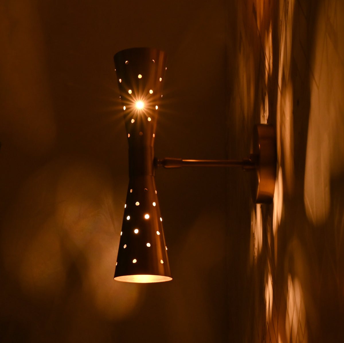 Side view of brass wall sconce glowing warmly against patterned wall
