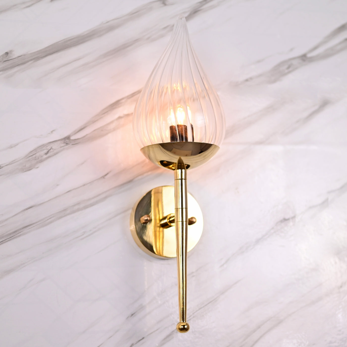 Polished brass wall sconce with teardrop glass shade mounted on white marble wall