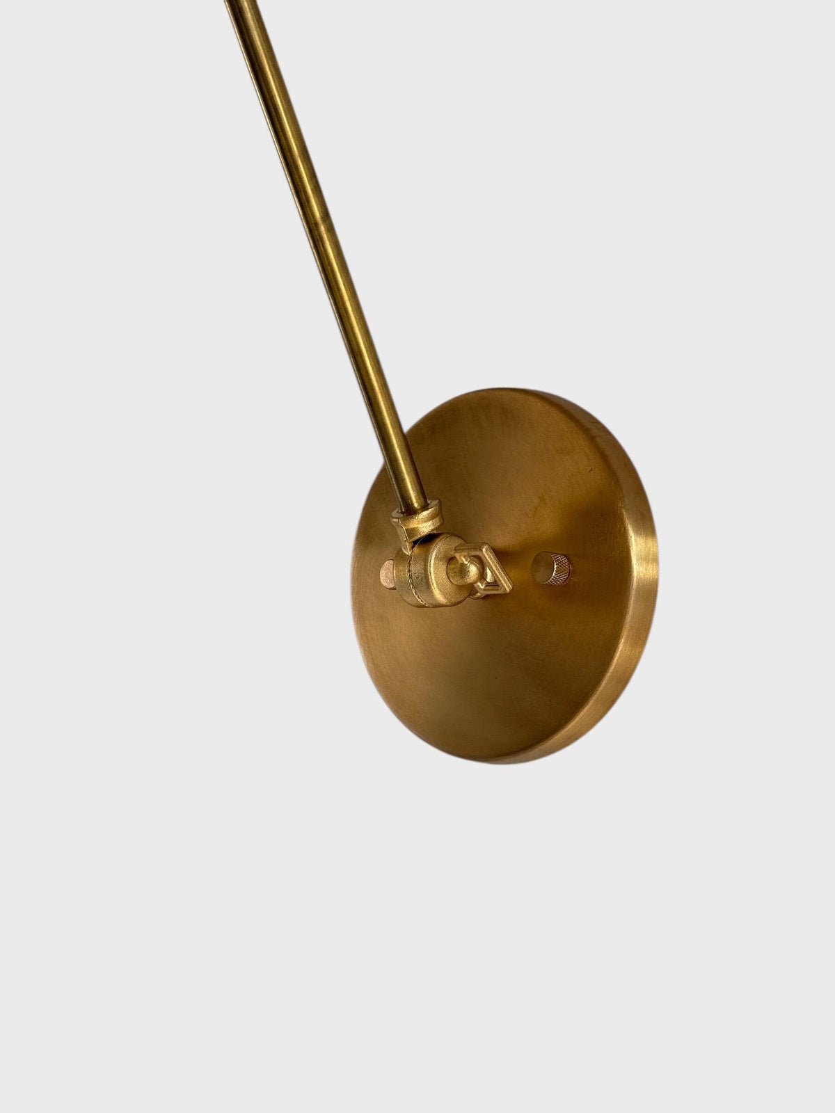 Close-up of round brass wall backplate and mounting area for adjustable swing arm wall light.