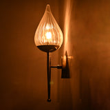 Close-up of lit brass wall sconce with sculpted teardrop fluted glass shade casting golden light