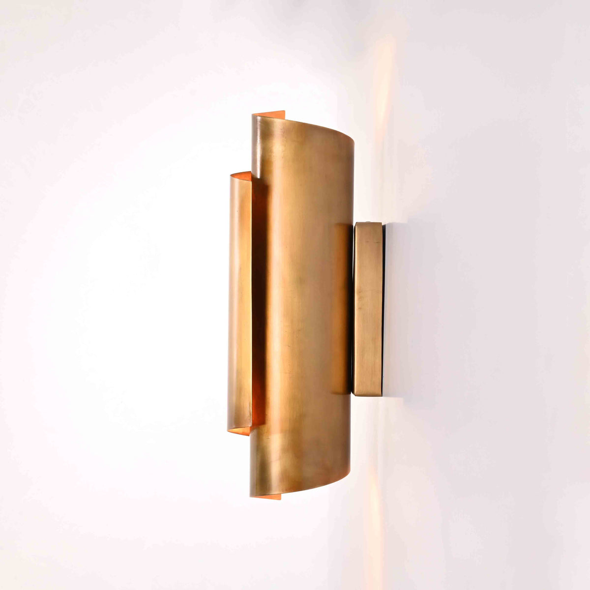 Brass wall sconce creating warm upward, downward, and side lighting effect on interior wall