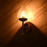 Warm glowing light from fluted glass teardrop sconce on brass base casting ambient shadows on marble wall
