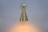 Front view of brass wall sconce with cone shade casting warm downward light, perfect for modern minimalist interiors.