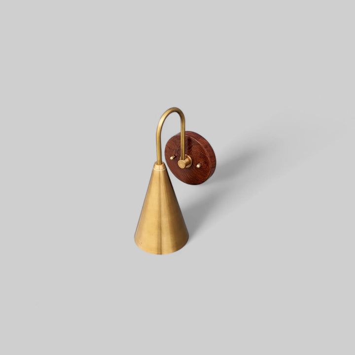 Top angle view of handcrafted brass and wood wall sconce showing curved arm and smooth satin brass cone shade.