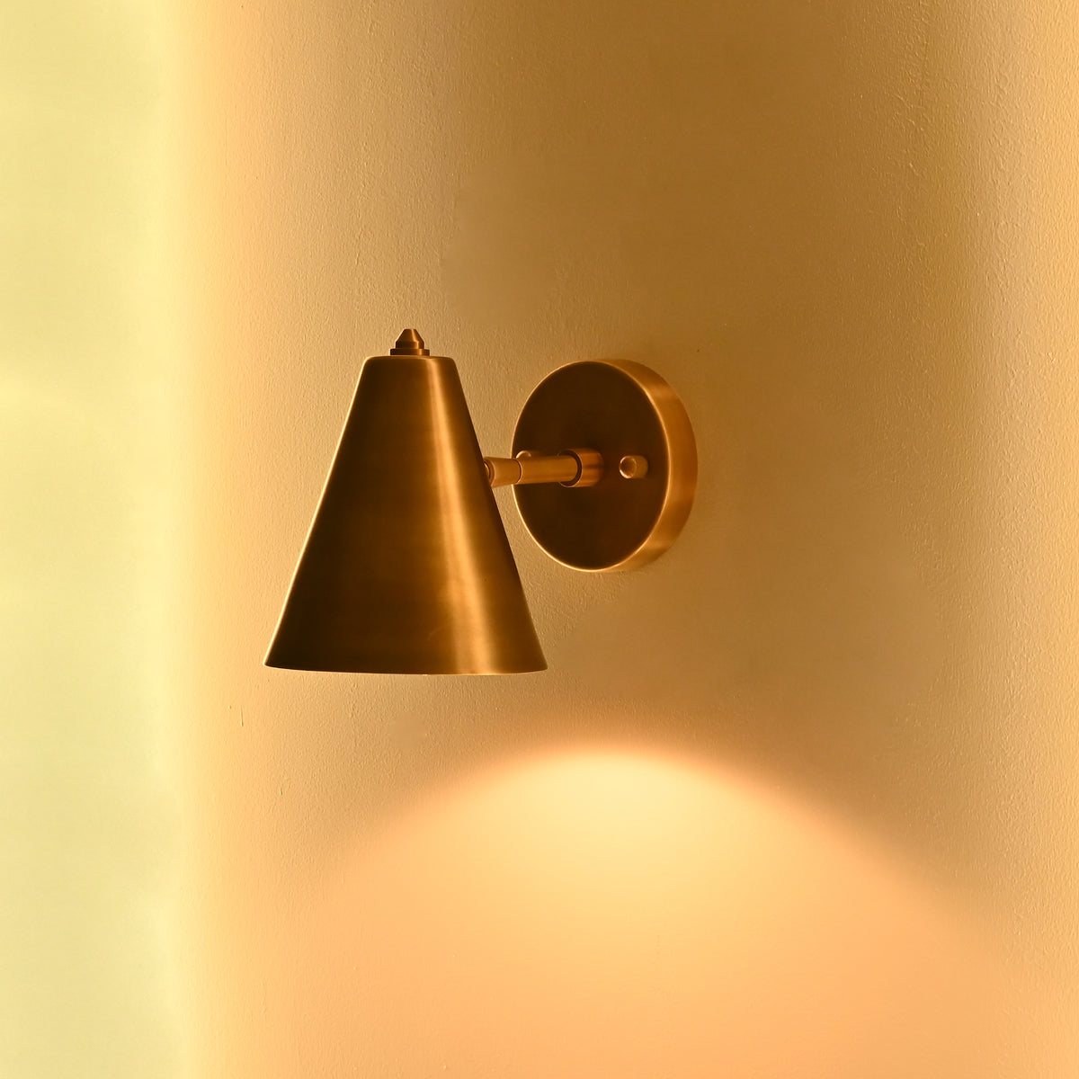 Small brass cone wall sconce styled beside a bathroom vanity mirror in a refined interior