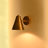 Small brass cone wall sconce styled beside a bathroom vanity mirror in a refined interior