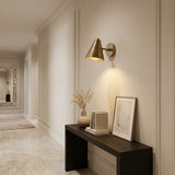 Brass cone wall sconce casting a warm focused downward glow on a neutral wall
