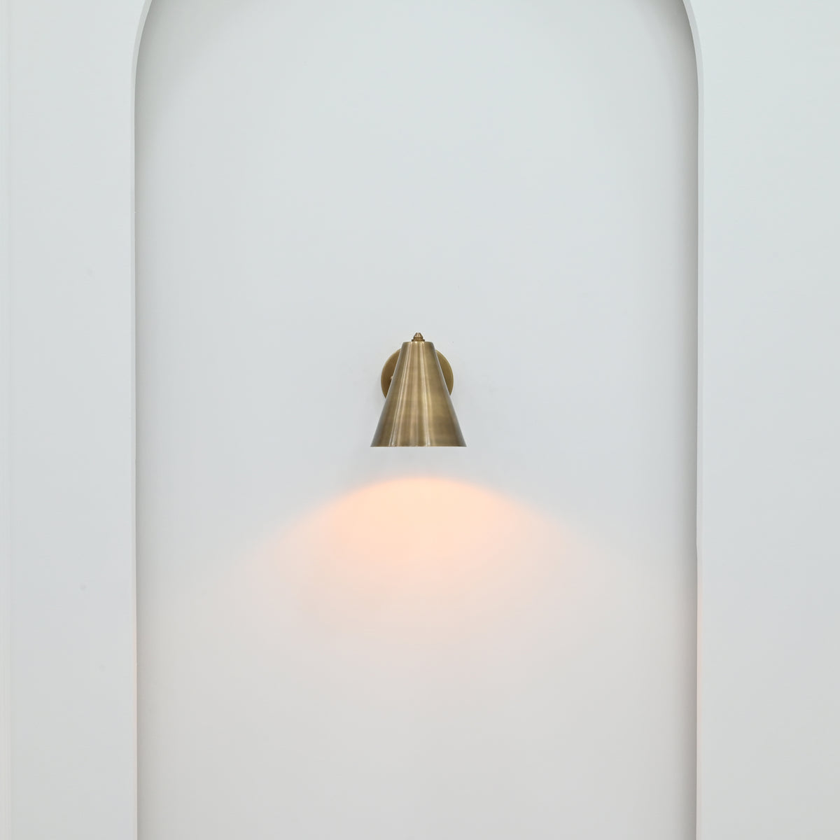 Compact brass patina wall sconce installed in an elegant hallway with warm directional lighting