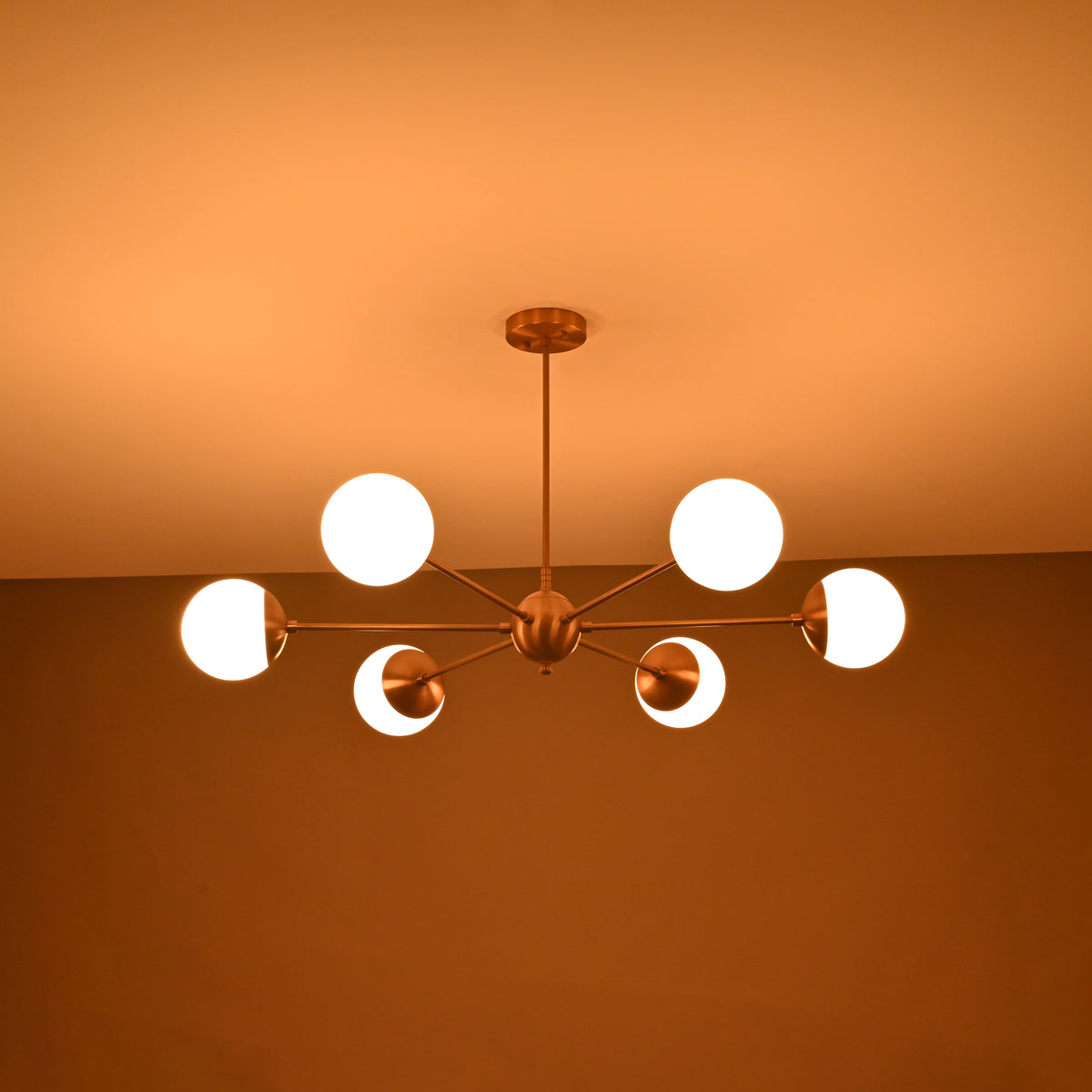 Elegant brushed brass chandelier with six illuminated globes creating warm evening ambient lighting.