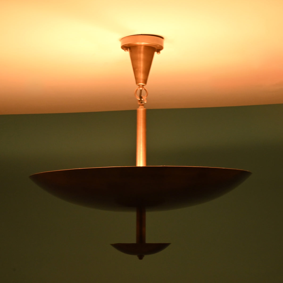 Brushed brass bowl disc chandelier illuminated with warm indirect lighting creating a soft ambient glow across the ceiling
