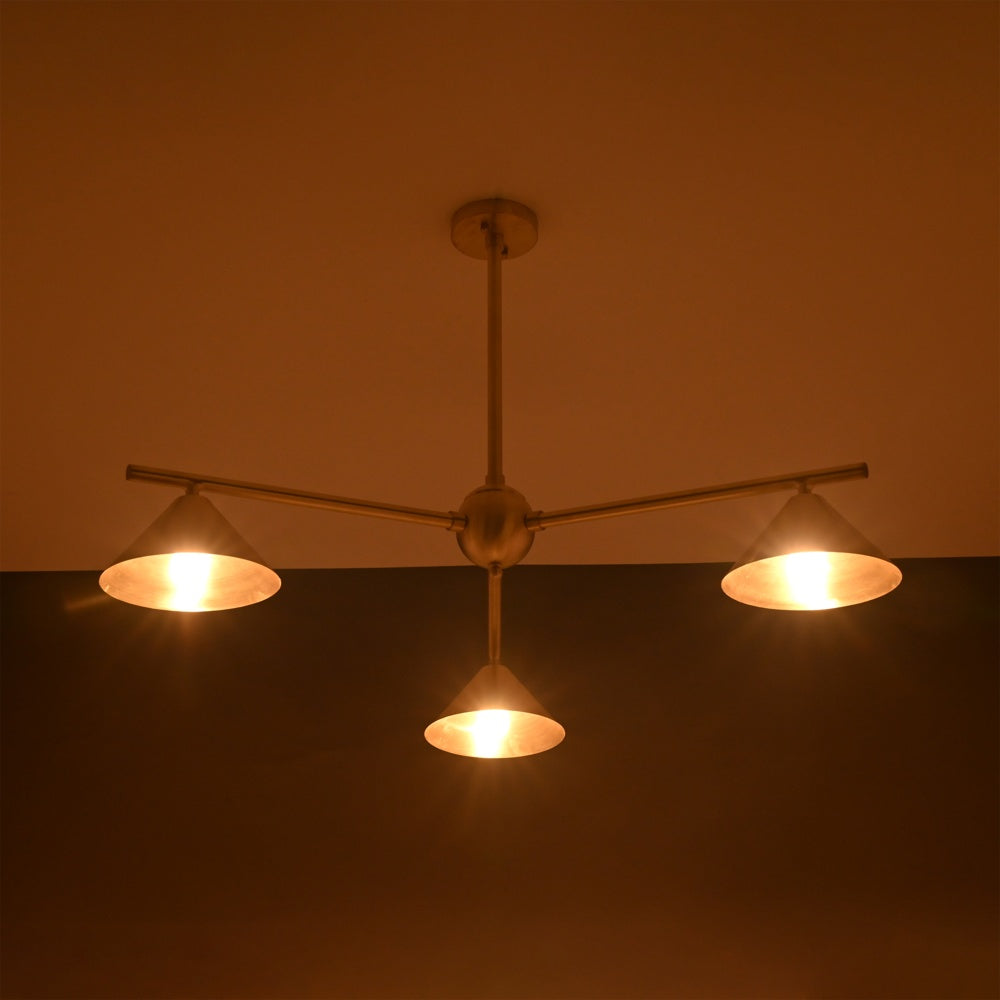 Warm-lit brushed brass chandelier with three cone shades, highlighting elegant sculpted industrial design.