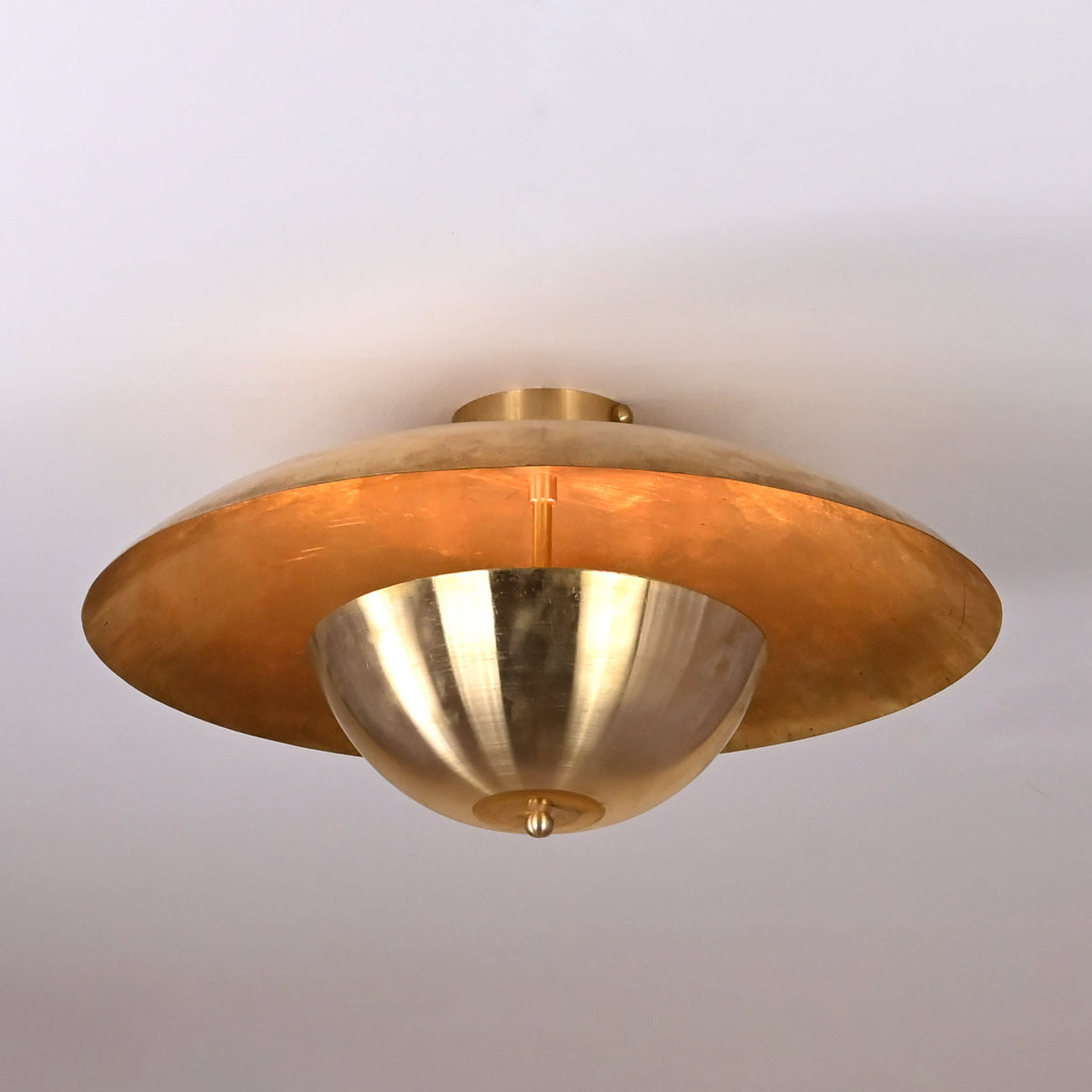 Close-up of brushed raw brass disc ceiling light showing smooth lacquered surface and warm golden tone