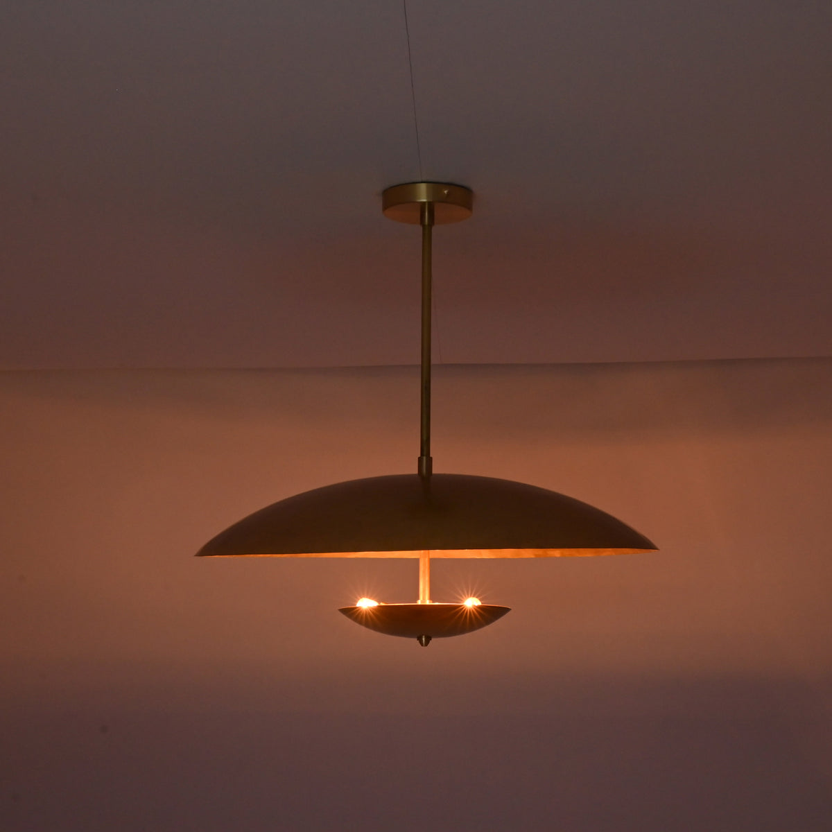 Brushed brass disc pendant illuminated in dark room creating soft indirect ambient lighting.