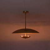 Brushed brass disc pendant illuminated in dark room creating soft indirect ambient lighting.