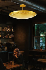 Brushed brass flush mount ceiling light illuminating a contemporary café seating area