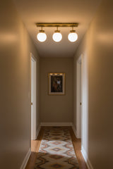 Brushed brass globe ceiling fixture with three white glass globes arranged in a clean linear design