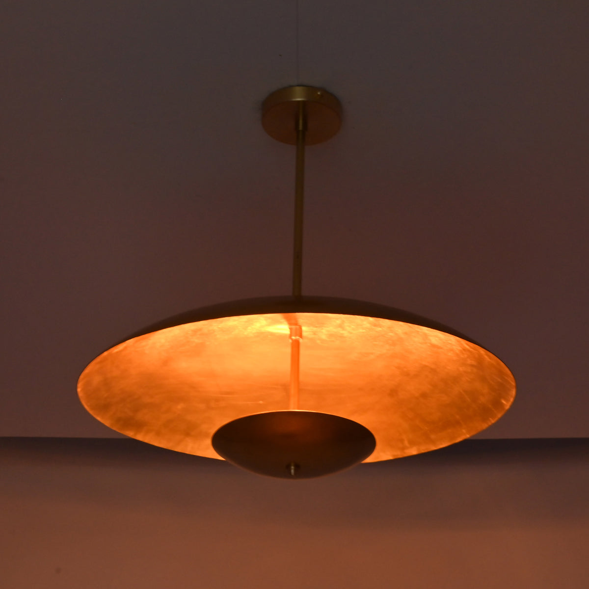 Underside view of brushed brass pendant showing warm reflected light and circular bowl form.