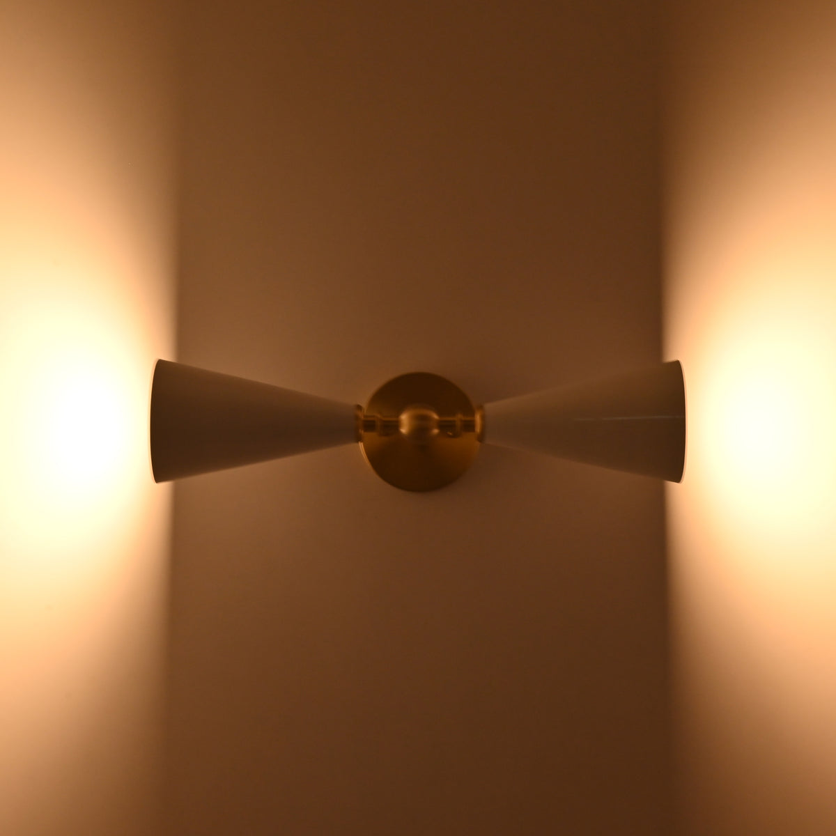 Brushed brass wall light closeup showing central sphere, arm detail, and white enamel cone shades