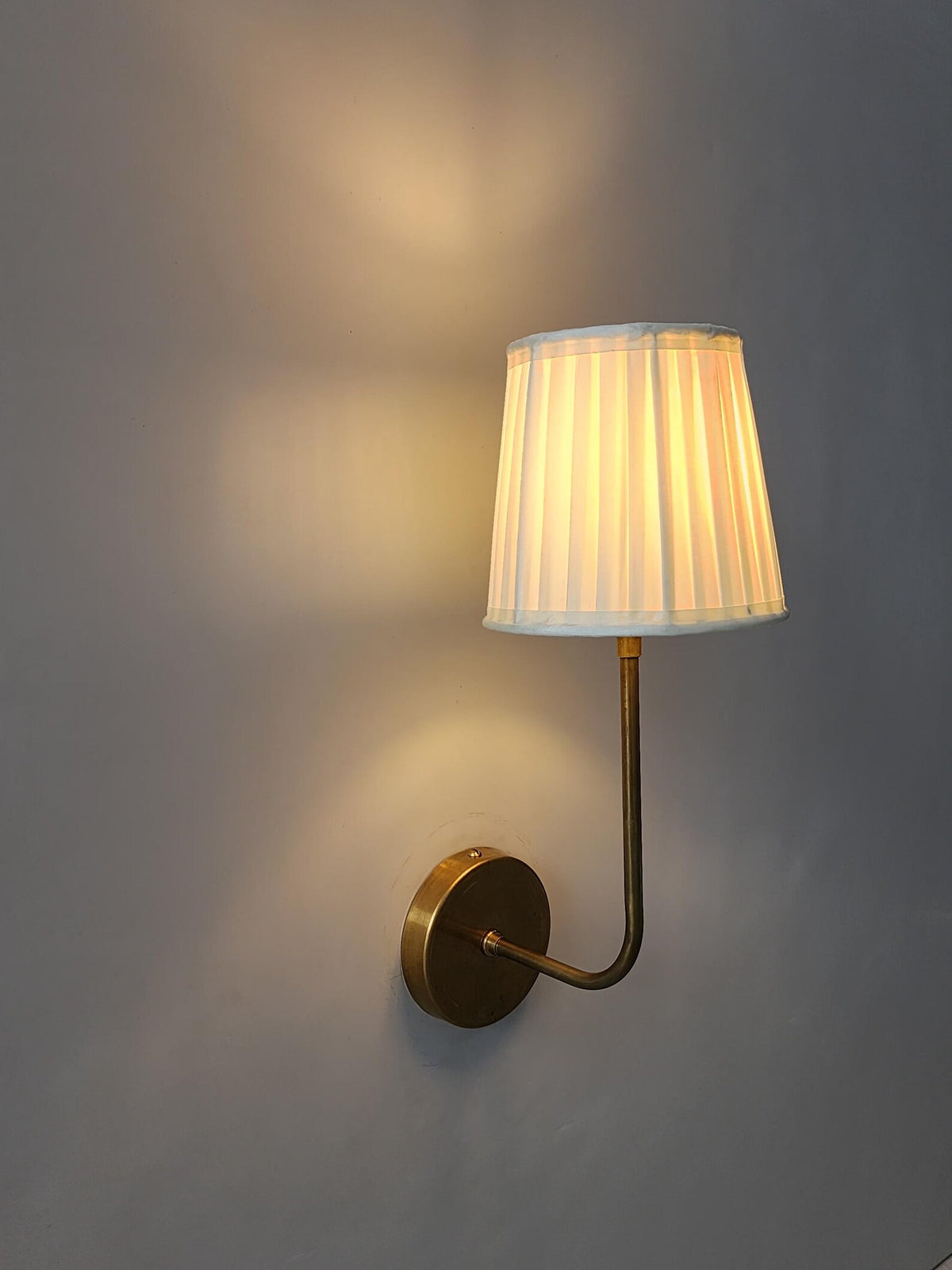 Close-up of brushed brass wall sconce highlighting the elegant pleated shade and fine craftsmanship.
