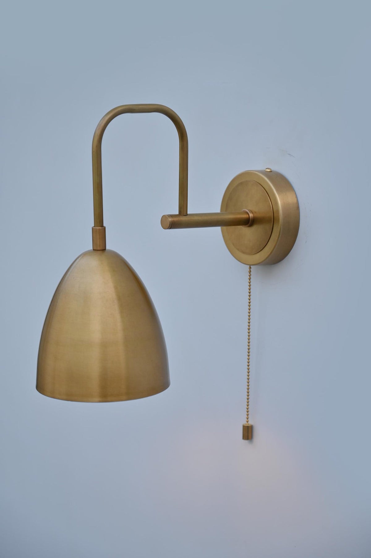 Close-up of brushed brass wall sconce showing dome shade and pull chain switch, handmade in solid brass with satin finish.