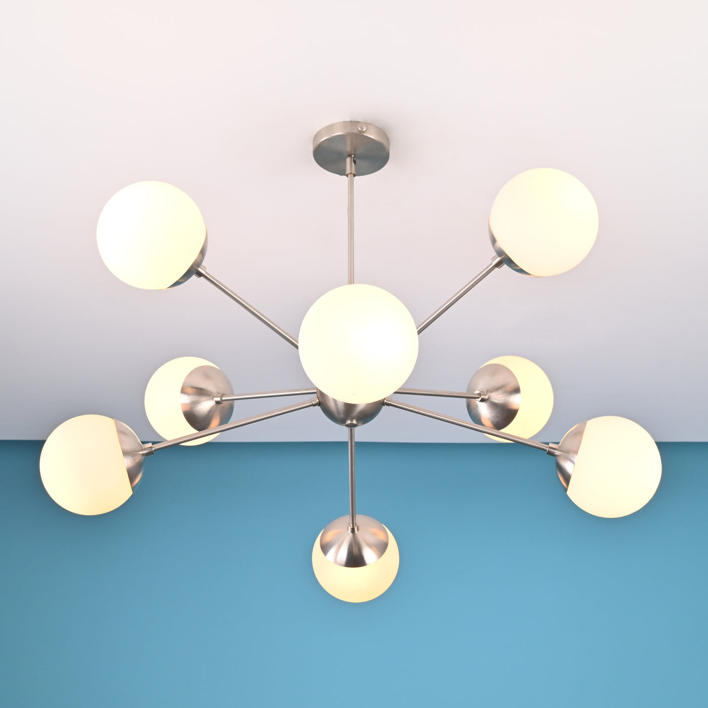Brushed nickel mid-century chandelier with eight globe shades installed on a white ceiling and blue accent wall.
