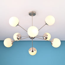 Brushed nickel mid-century chandelier with eight globe shades installed on a white ceiling and blue accent wall.
