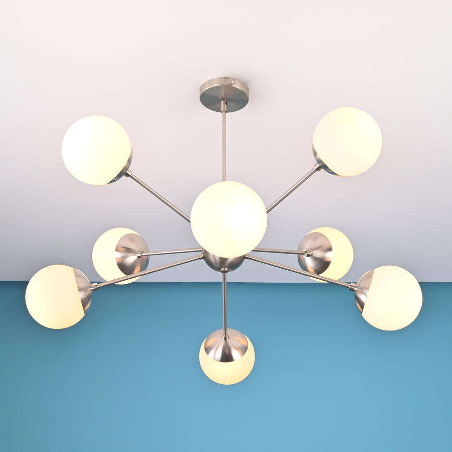 Brushed nickel mid-century chandelier with eight globe shades installed on a white ceiling and blue accent wall.