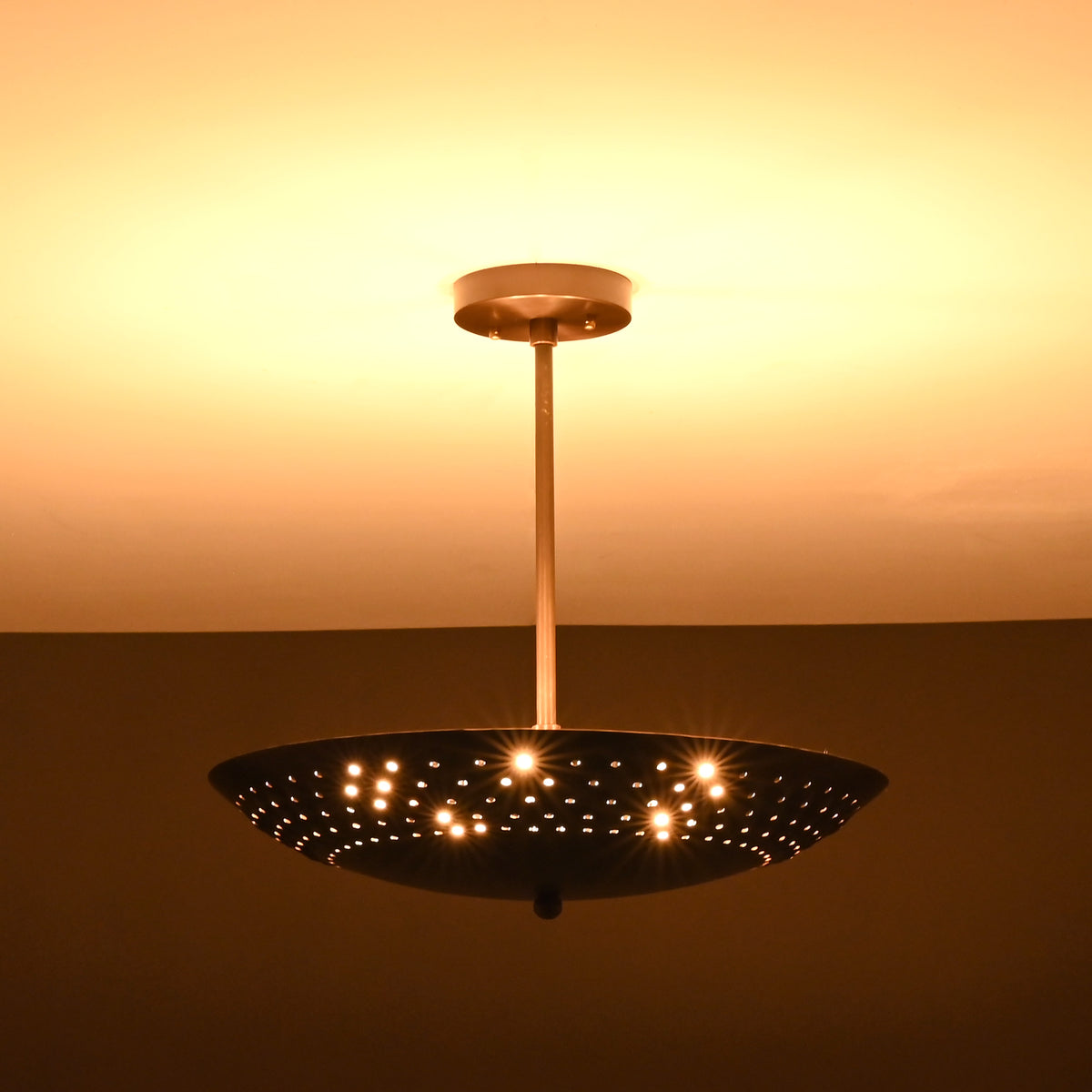 Brushed brass disc ceiling light illuminated with perforated design pattern