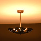 Brushed brass disc ceiling light illuminated with perforated design pattern