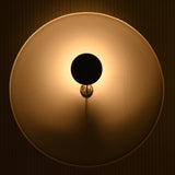 Blackened brass accent wall light with rounded disc shade and warm reflected illumination