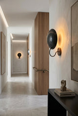 Curved disc wall light in blackened brass with sculptural profile and soft ambient glow
