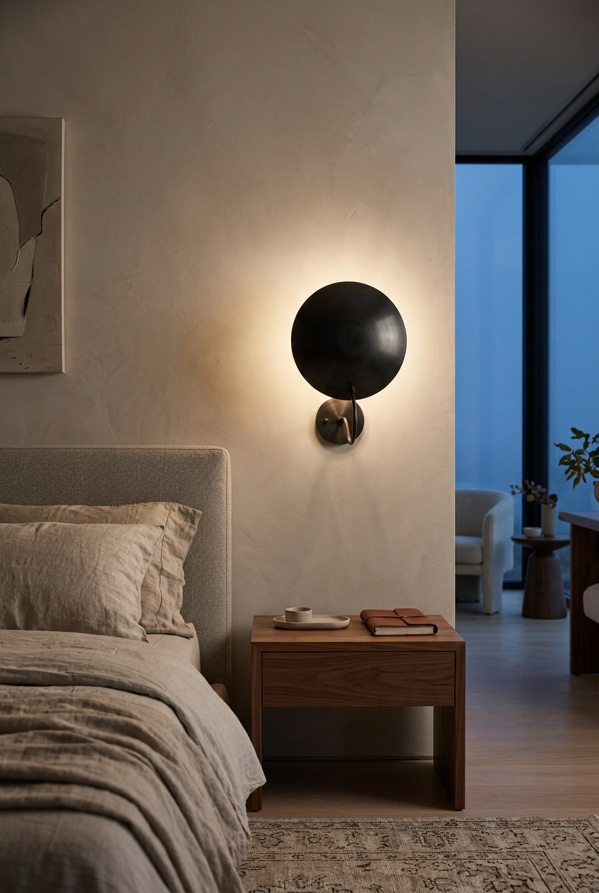 Modern indirect wall sconce with blackened brass disc shade and curved support arm