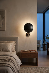 Modern indirect wall sconce with blackened brass disc shade and curved support arm