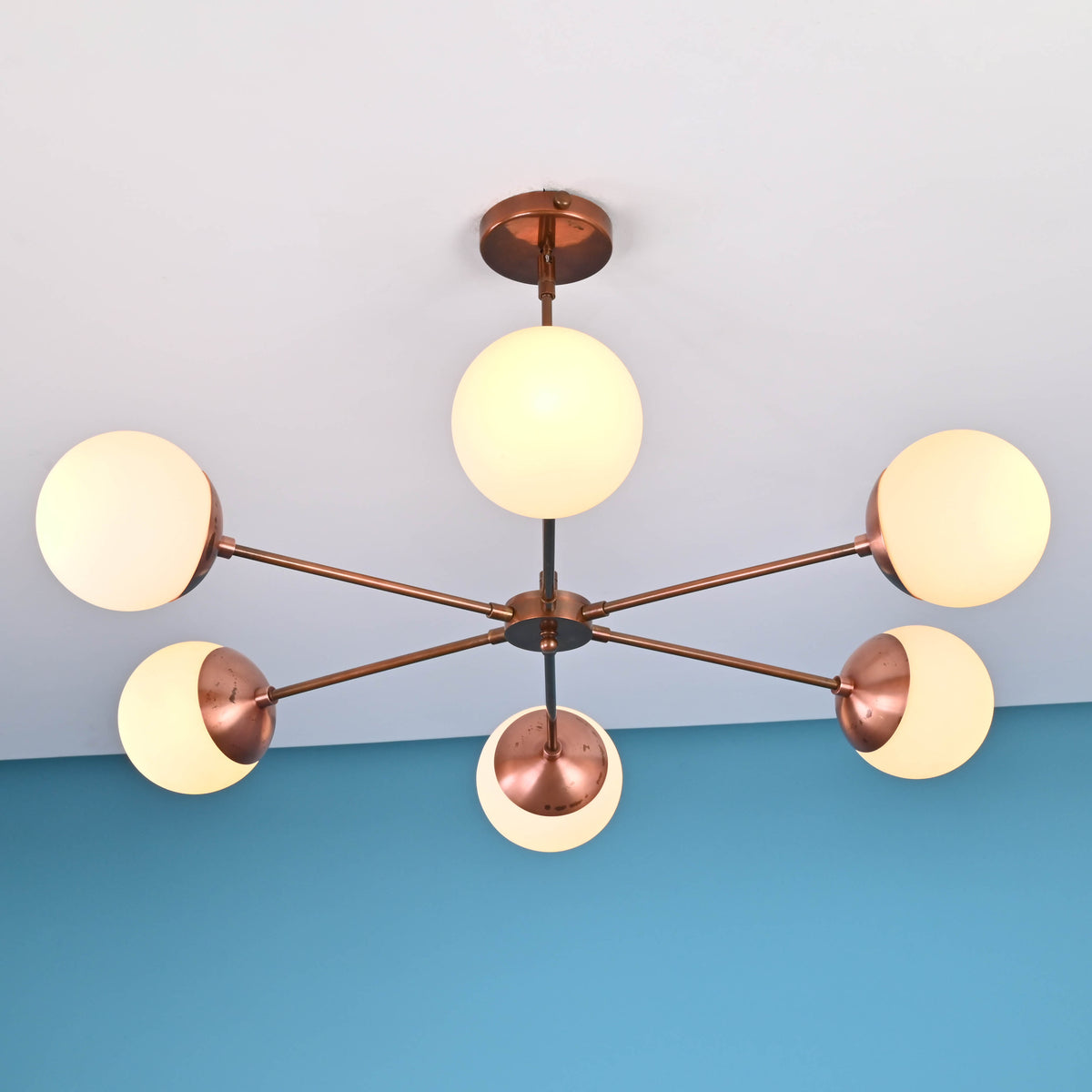 Close-up view of modern brass chandelier with six frosted glass globes and copper-toned arms mounted on ceiling.