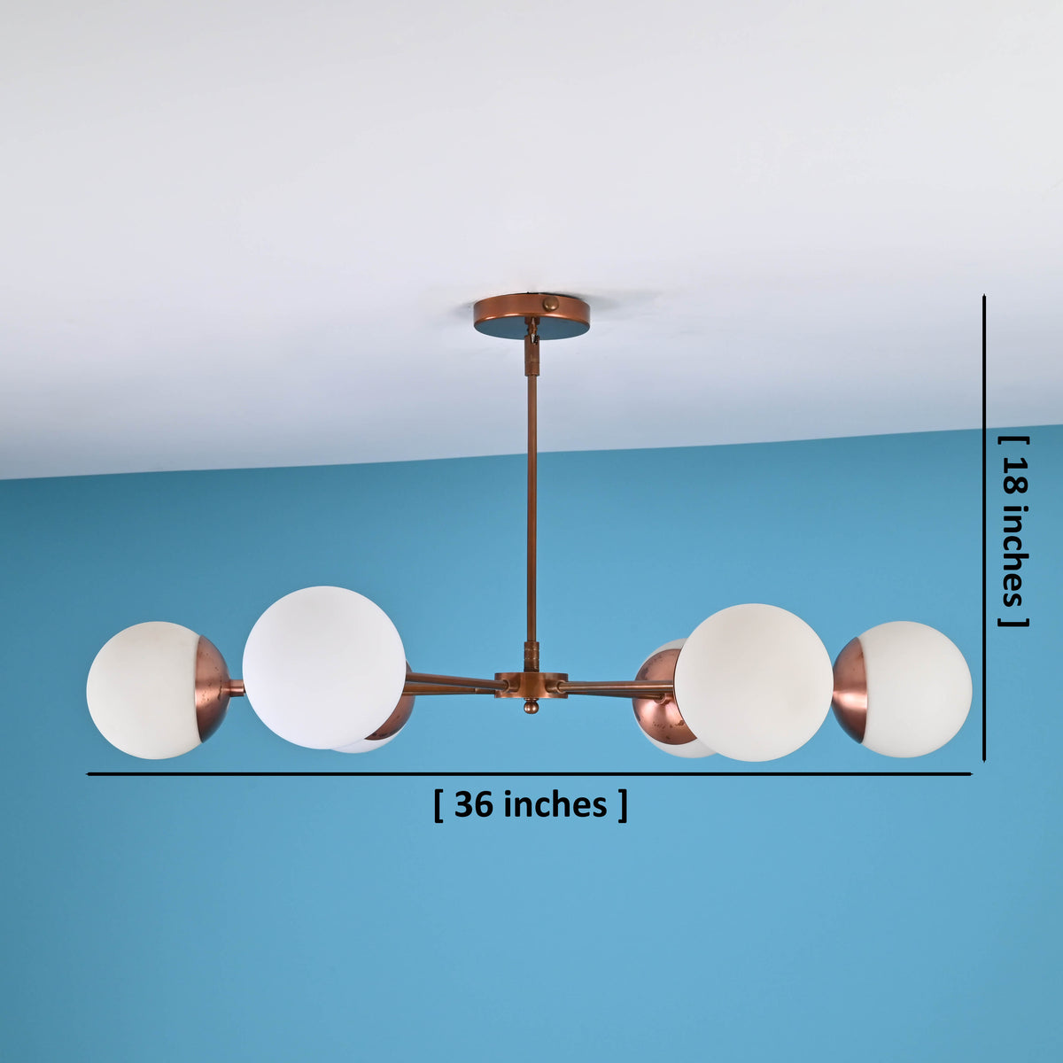 Modern brass chandelier with frosted glass globes showing 36-inch width and 18-inch height measurements against blue wall background.