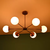 Modern brass chandelier with six frosted glass globes glowing warmly on ceiling in a dimly lit room.