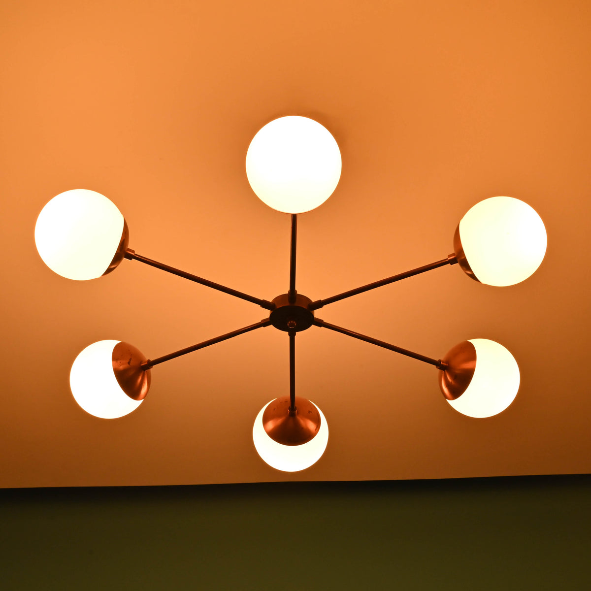 Six-light brass chandelier illuminated, creating warm ambient glow with frosted glass globes and copper accents.