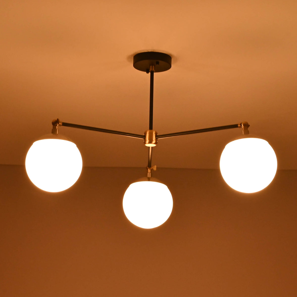 Modern brass and black flushmount chandelier glowing warmly with three globe lights