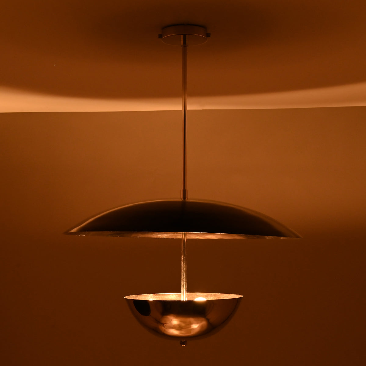 Chrome bowl-and-disc pendant light producing warm indirect illumination from below