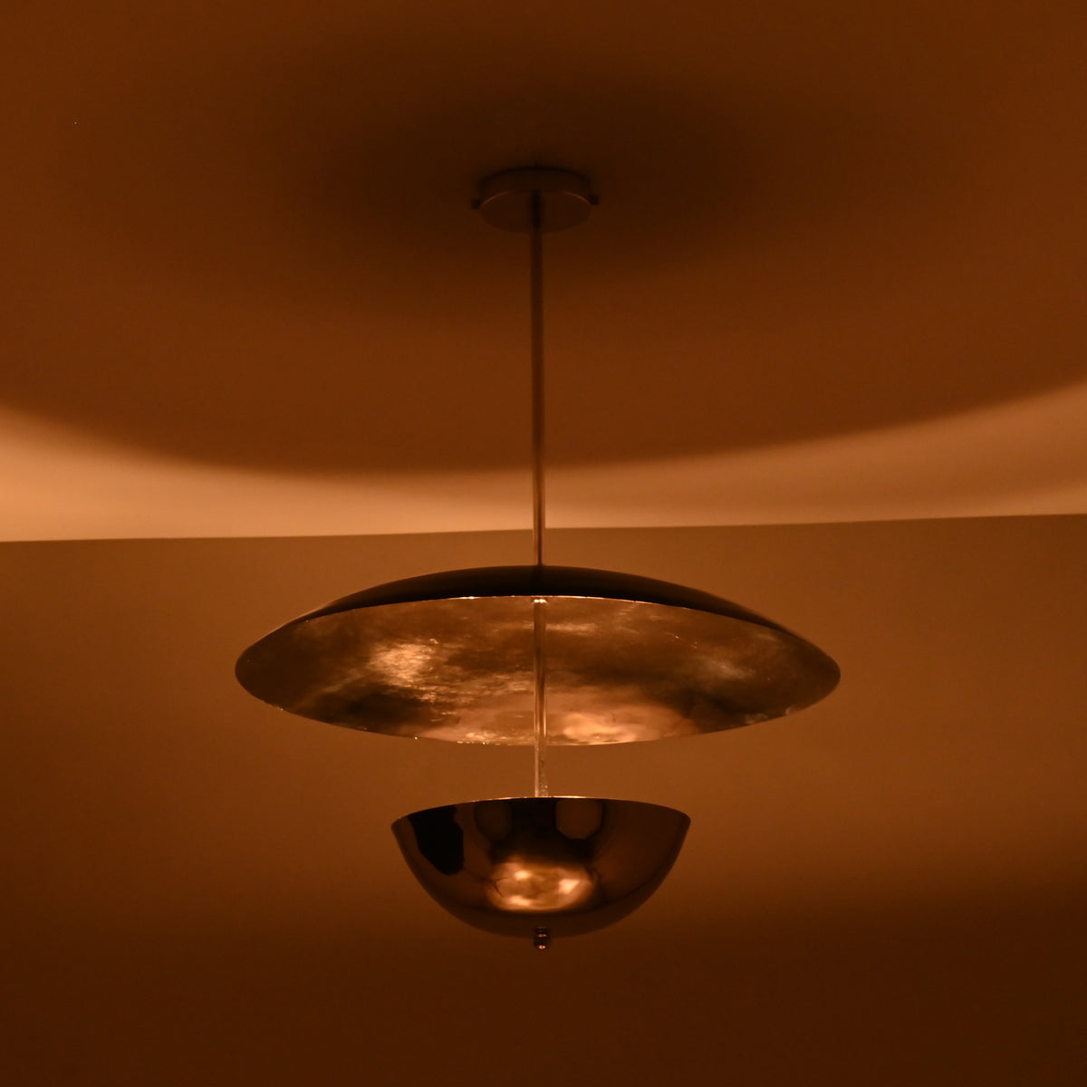 Chrome brass disc chandelier illuminated at night with warm ambient lighting and soft reflections