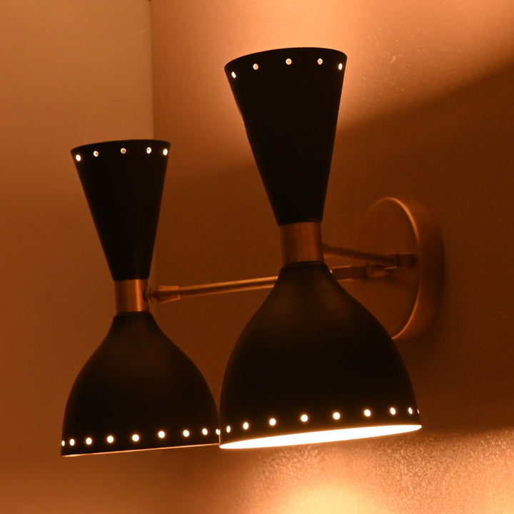 Close-up of double brass black cone wall sconce emitting warm light