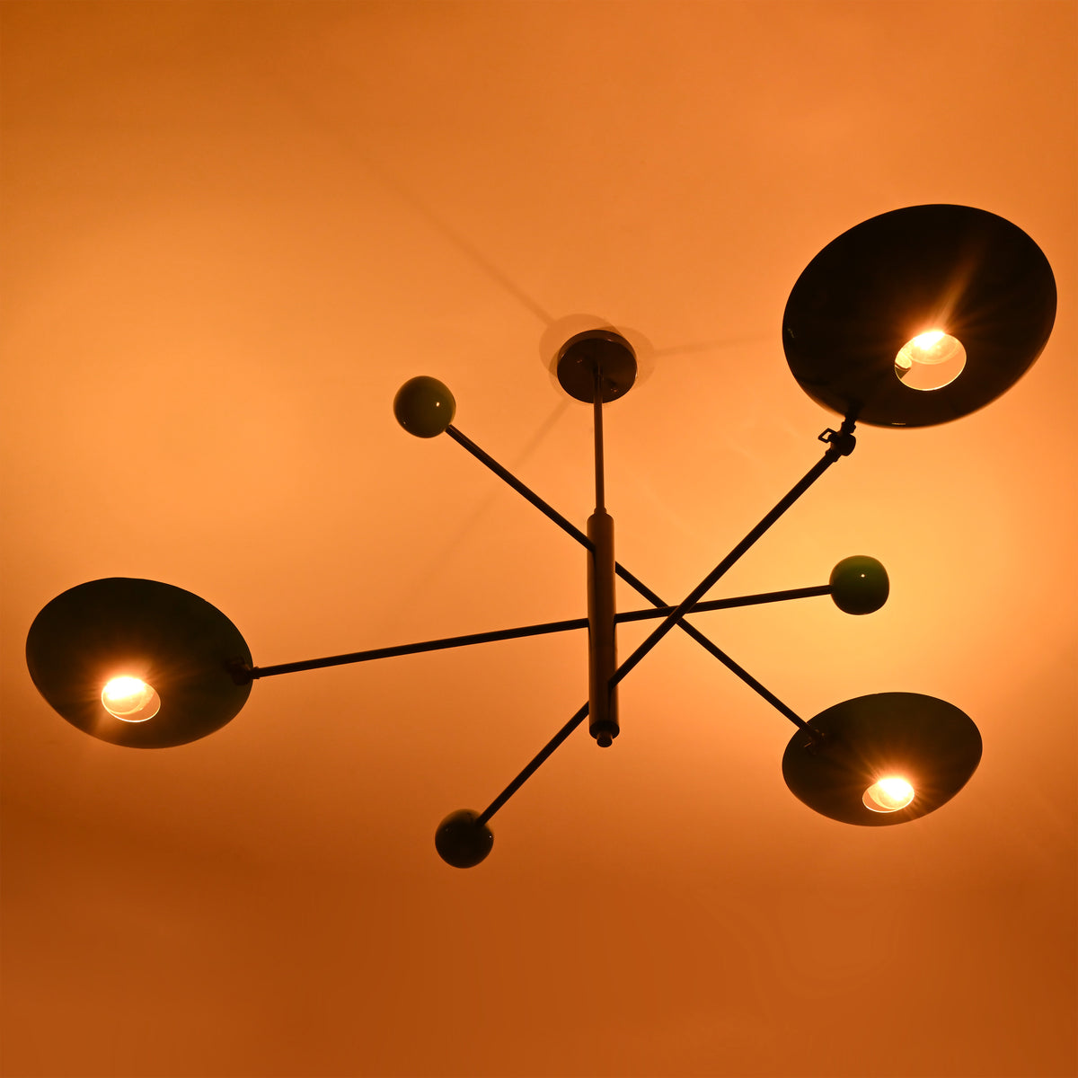 Warm glowing Sputnik-style chandelier with bold disc shades in green tones, casting ambient light in a dark room