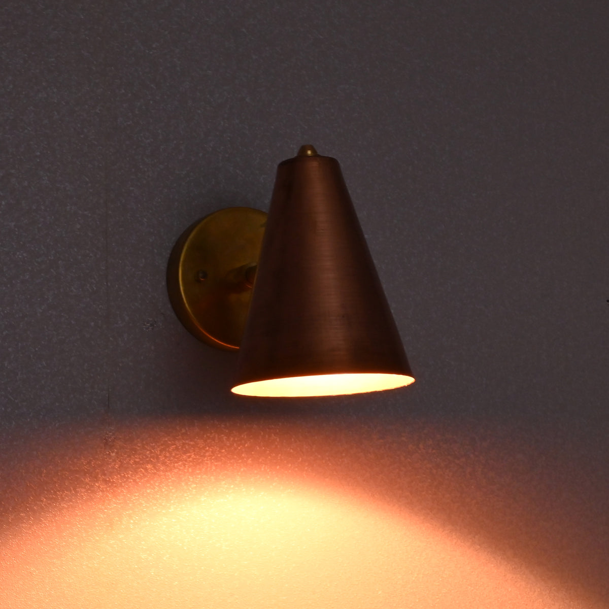 Cone-shaped copper shade wall lamp in brass finish, illuminated in low light ambiance.