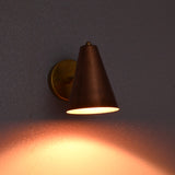Cone-shaped copper shade wall lamp in brass finish, illuminated in low light ambiance.