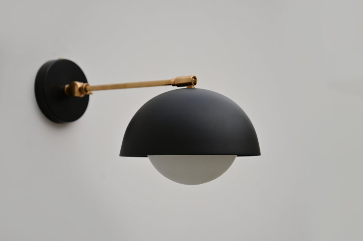 Front view of contemporary black dome wall light with brass fixture, combining industrial and minimalist design elements.