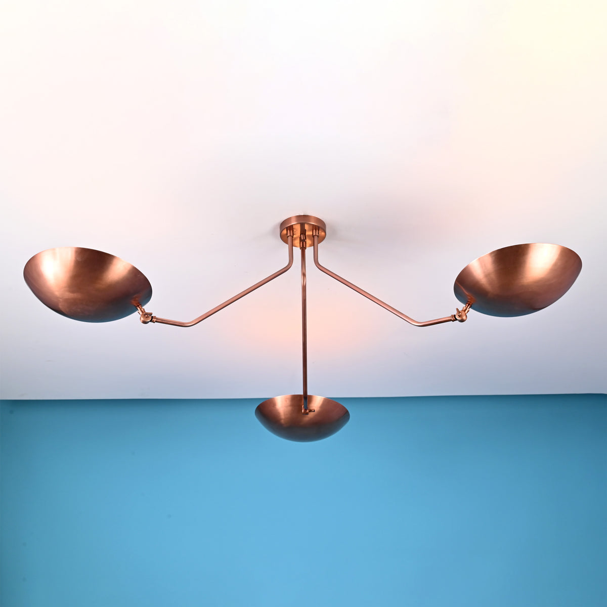 Copper 3-light flushmount chandelier with bowl shades against a blue wall background.