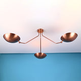 Copper 3-light flushmount chandelier with bowl shades against a blue wall background.