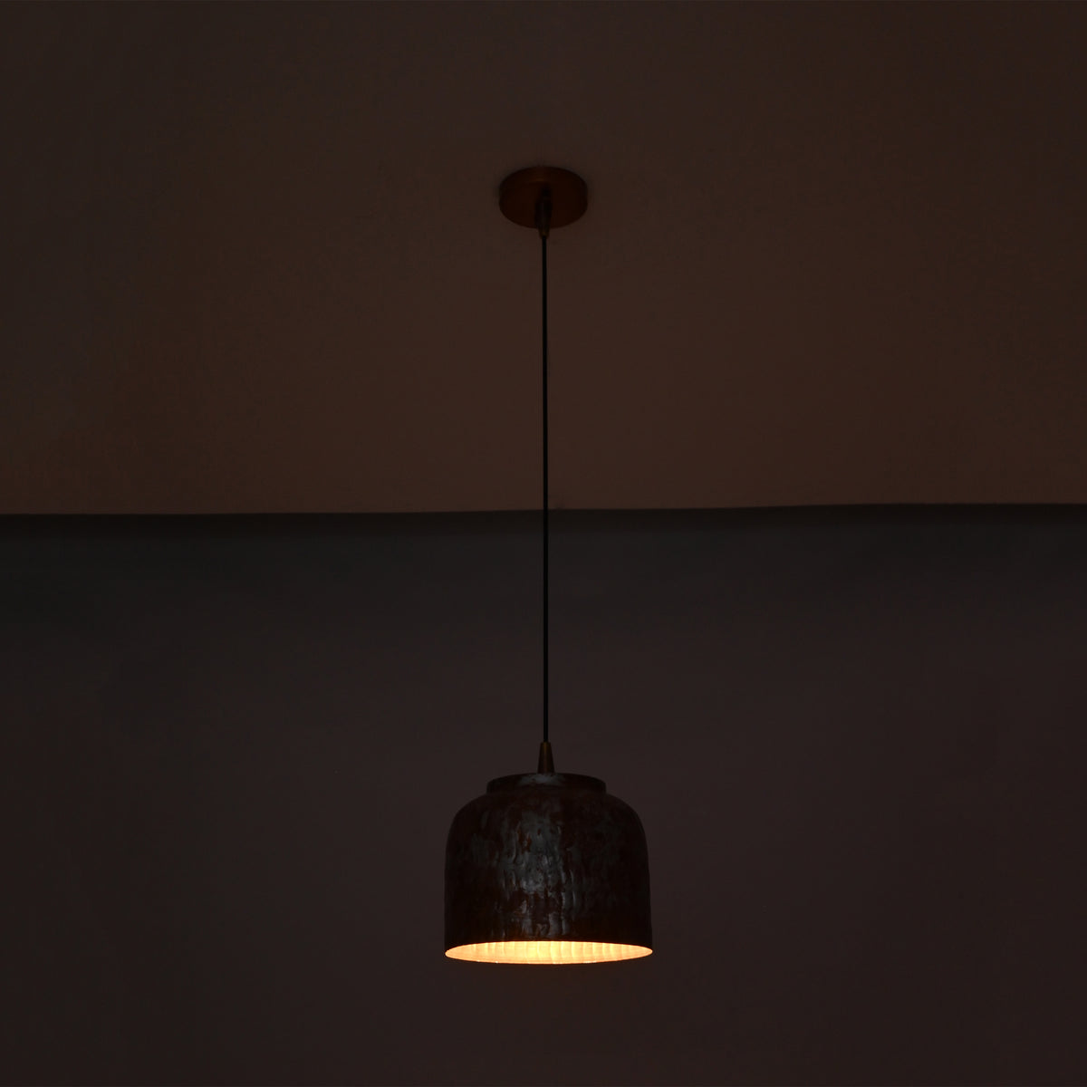 Cora pendant light glowing warmly from below, highlighting the compact drum shade and textured copper finish