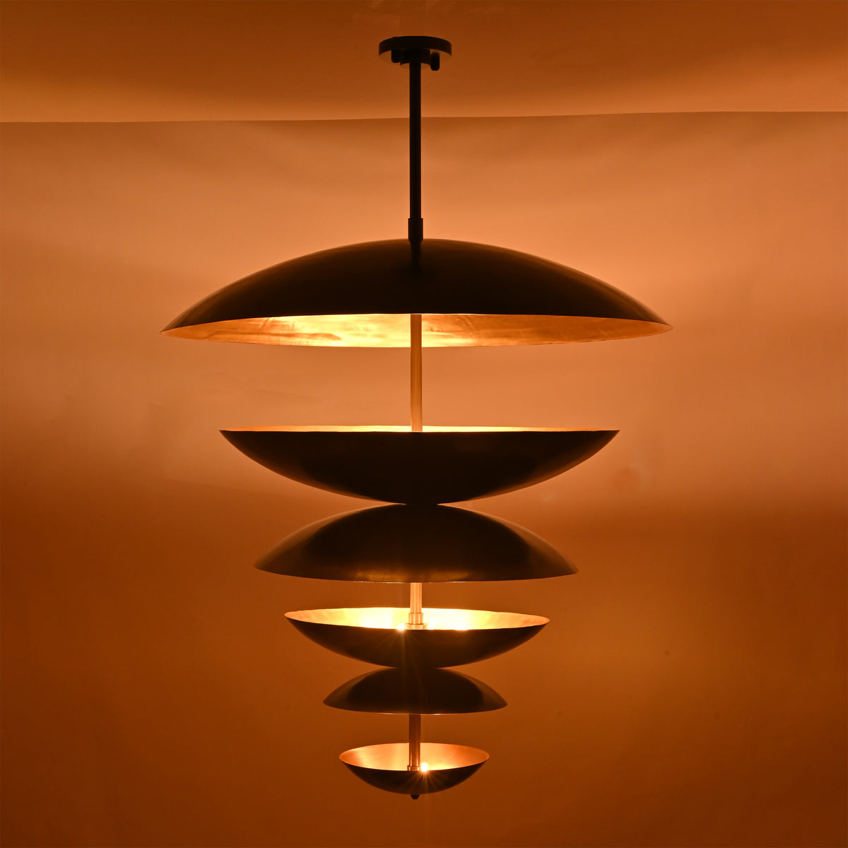 Solid brass disc chandelier displayed in a covered lounge space with warm reflected light and sculptural ceiling presence
