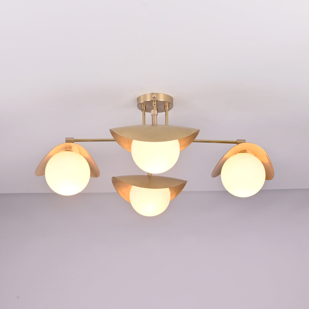 Lit front view of Curva brass flush mount featuring warm ambient glow, curved brass shades, and minimalist globe design.